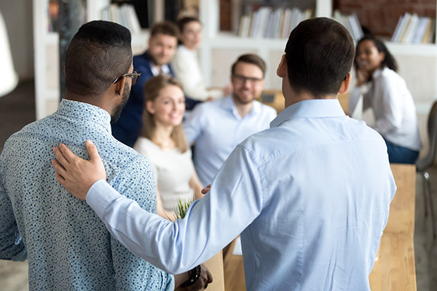 Two male co workers being celebrated in a company meeting