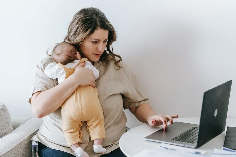 Remote employee holding a baby while working on her laptop