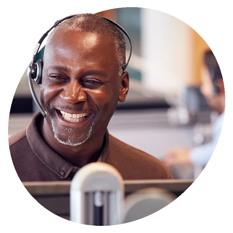 Smiling customer service representative wearing a headset, seated at a desk in a modern office environment.