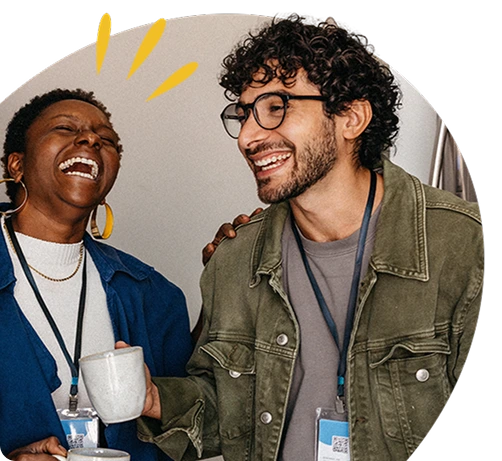 Two coworkers laughing and enjoying coffee together at a workplace event, wearing ID lanyards.
