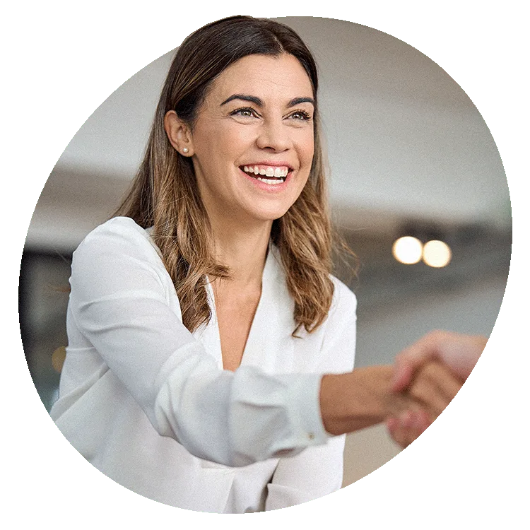 Smiling professional woman in a white blouse shaking hands in a modern office setting, representing successful business partnership or onboarding.