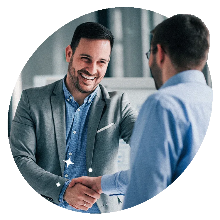 Two business professionals smiling and shaking hands in an office setting, symbolising successful partnership and collaboration.