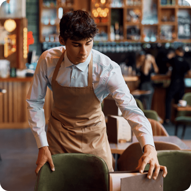Young hospitality worker setting up a restaurant table, representing frontline employees who benefit from practical, morale-boosting benefits.