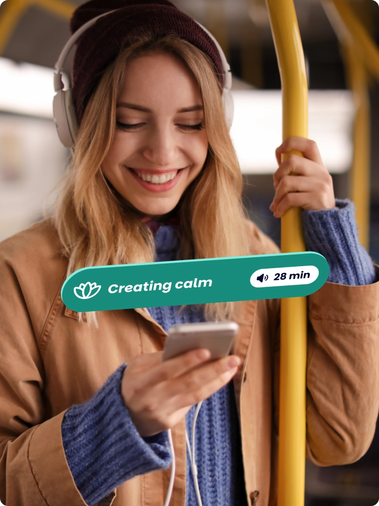 Woman wearing a beanie and headphones smiling at her phone on a bus, with a 'Creating calm, 28 min' audio label overlaid.